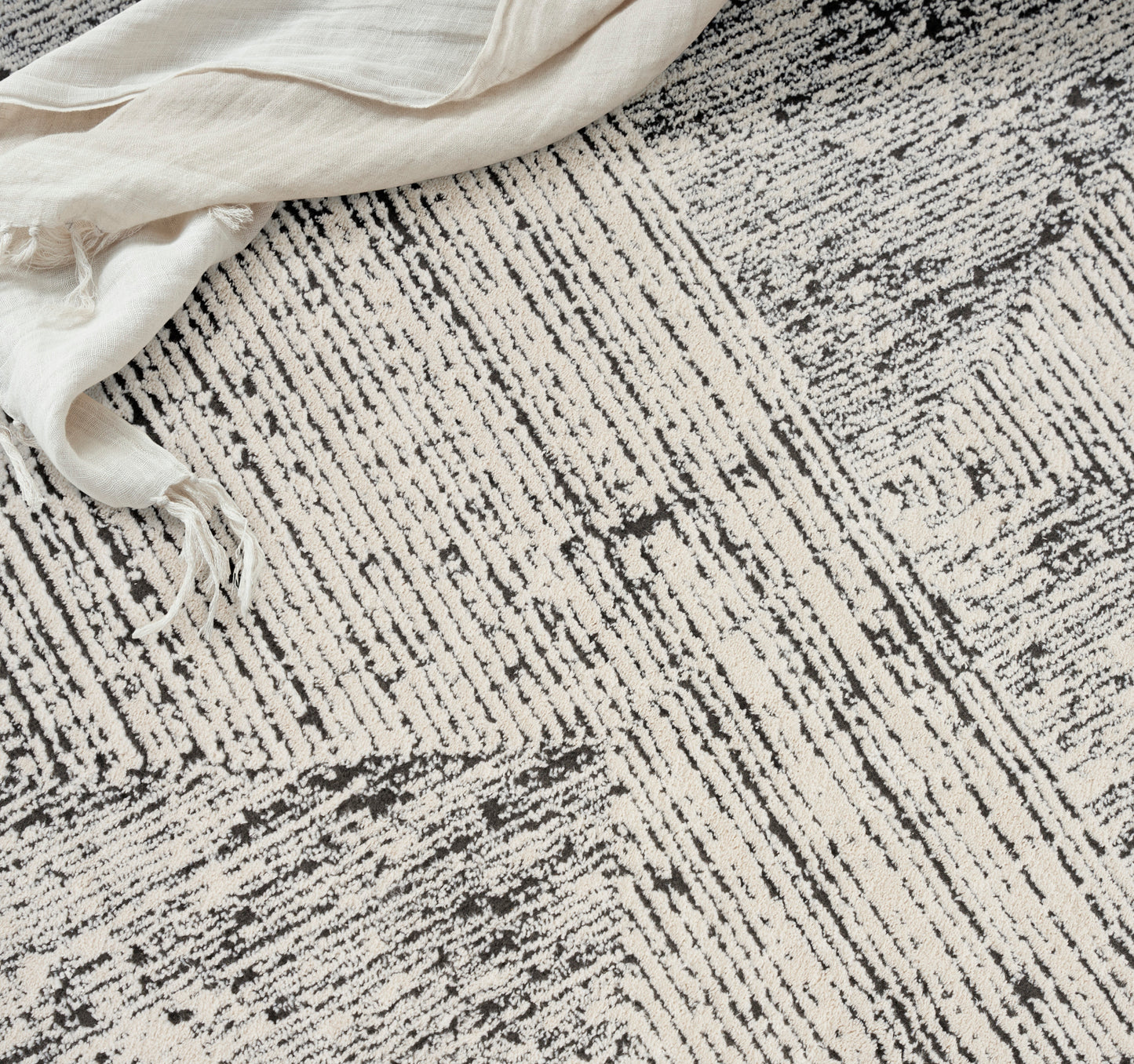 Beige-gray textured rug with irregular linear stripes and a cream linen cloth draped at the corner.