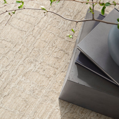 Beige textured rug with a gray concrete coffee table, stacked gray magazines, a blue bowl, and trailing green vine.