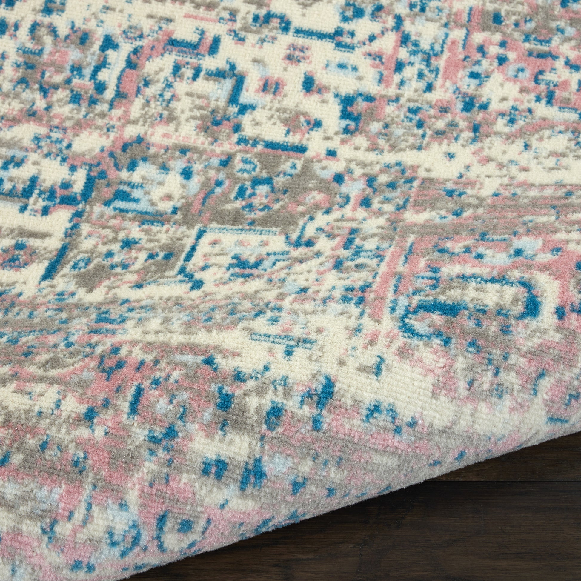 Distressed pink, blue and ivory patterned area rug with geometric motifs on a dark wood floor.
