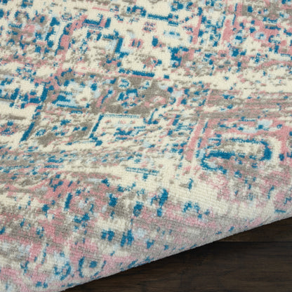 Distressed pink, blue and ivory patterned area rug with geometric motifs on a dark wood floor.