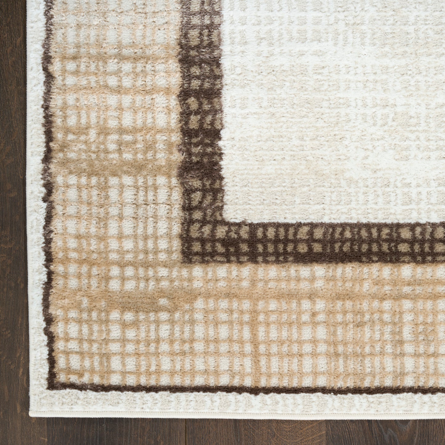 Beige rectangular area rug with cream center, dark brown border and subtle grid texture on wood floor