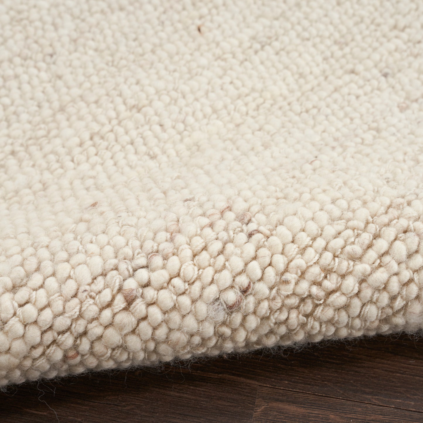 Cream boucle rug with dense loop pile & chunky tufts, edge folded on dark wood floor.