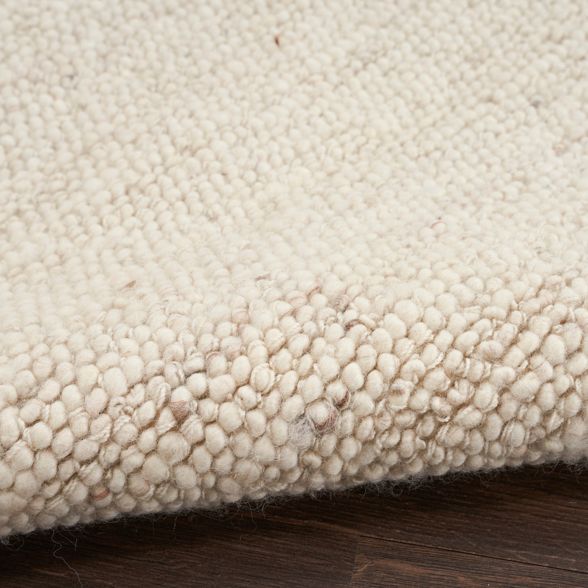 Cream boucle rug with dense loop pile & chunky tufts, edge folded on dark wood floor.