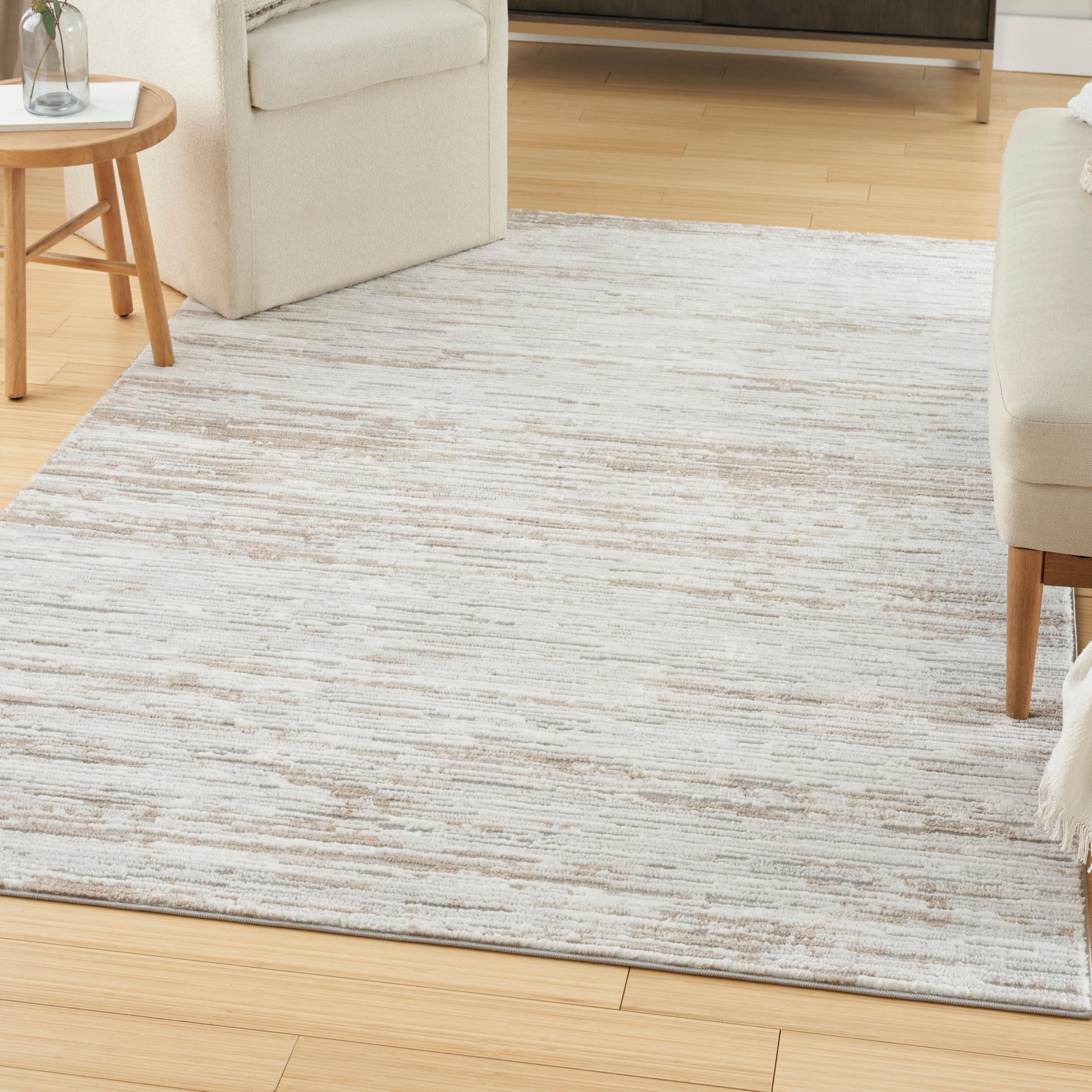Light beige and gray abstract area rug on light wood floor, paired with cream sofa and round wooden side table with plant.