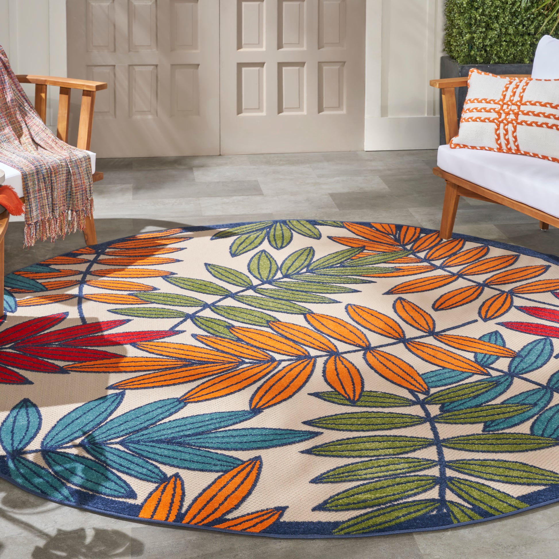 Round rug with vibrant multicolor leaf pattern (orange, green, blue) on a porch, flanked by wooden chairs.