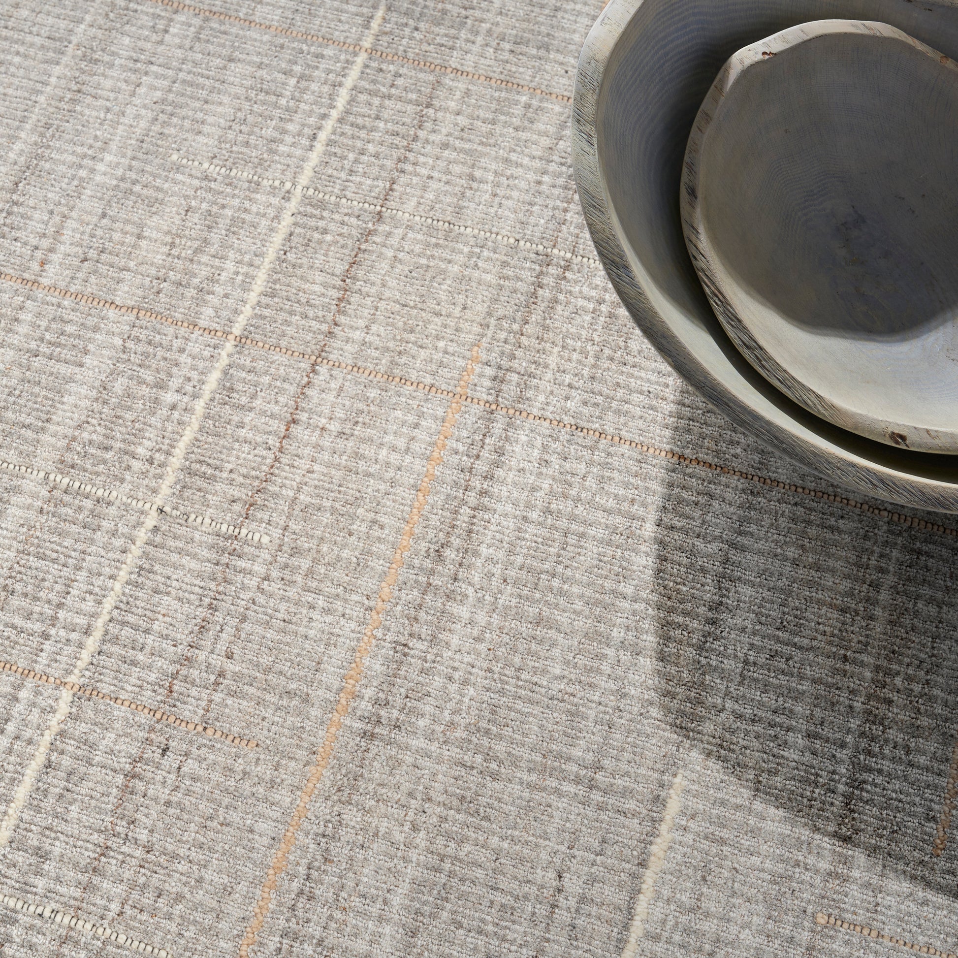 Neutral gray woven rug with tan grid lines; stacked round ceramic bowls in the corner.