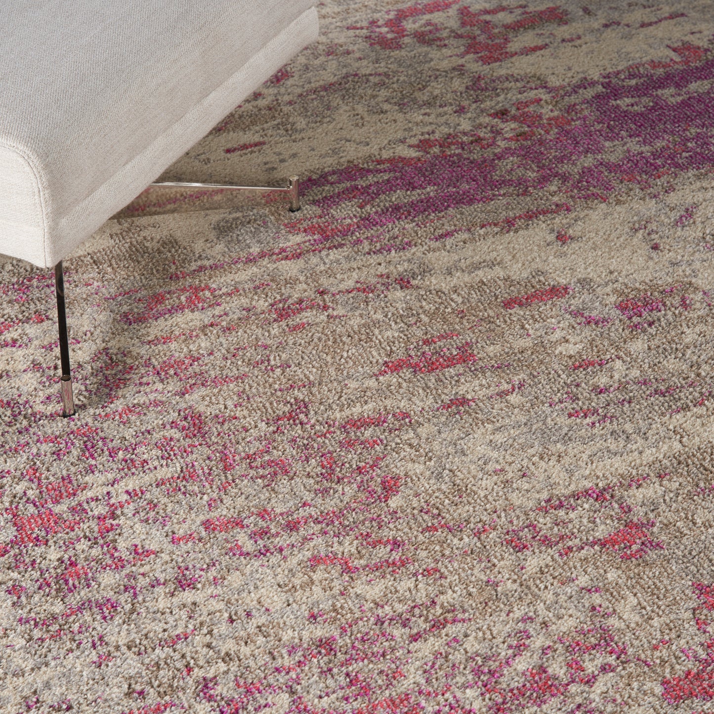 Beige area rug with pink and magenta accents under a light gray upholstered sofa with metal legs.