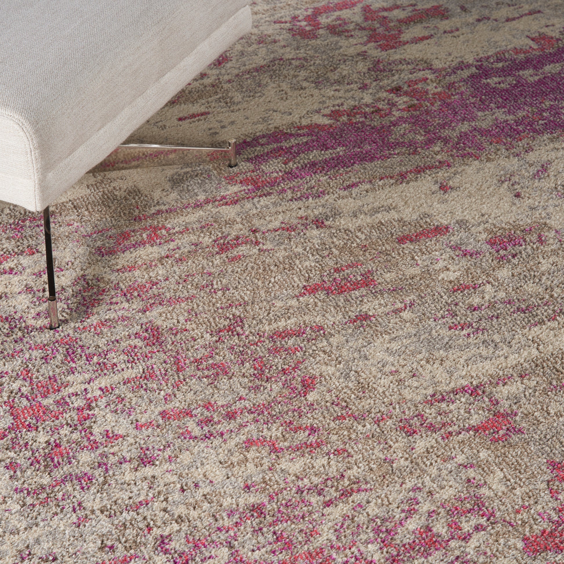Beige area rug with pink and magenta accents under a light gray upholstered sofa with metal legs.