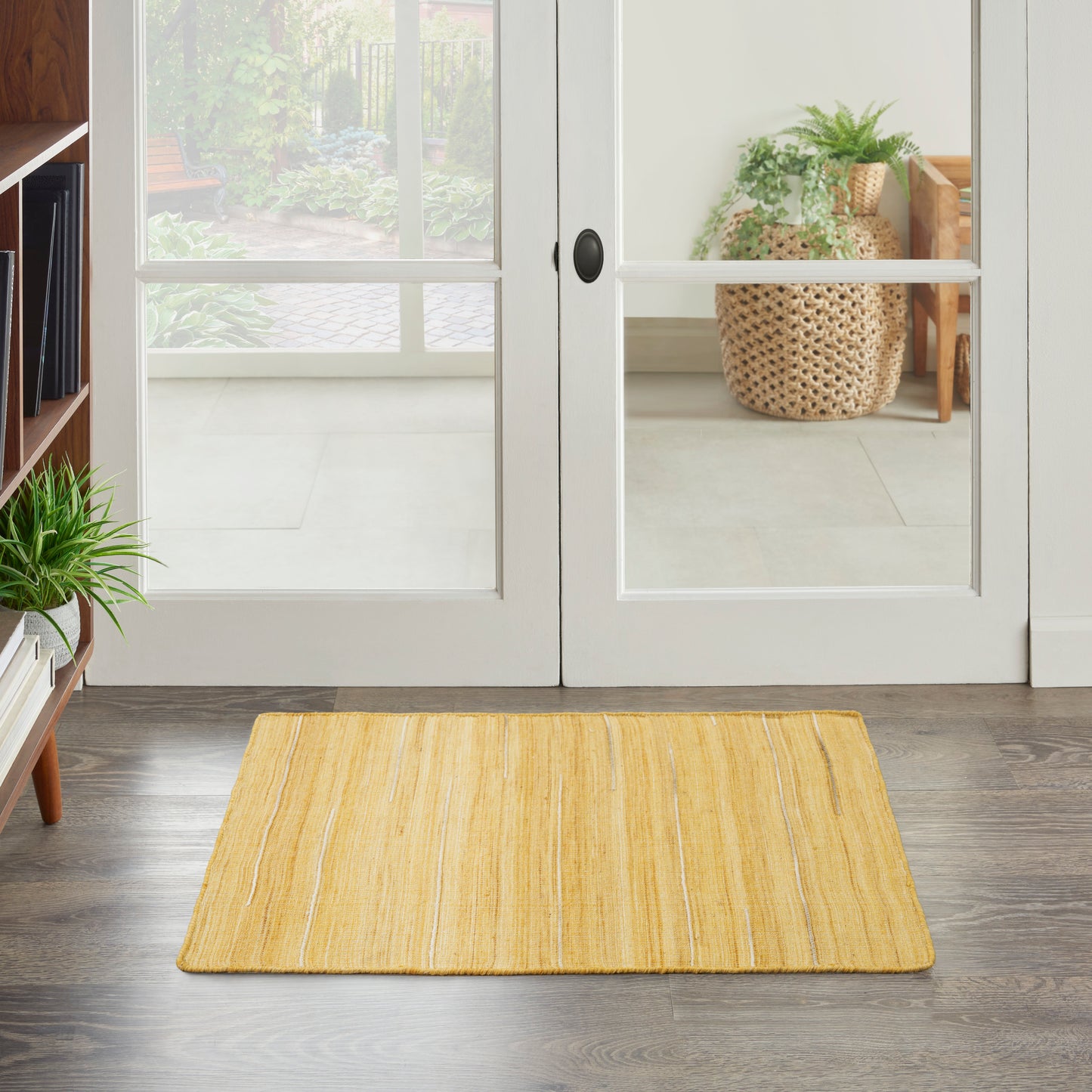Yellow woven entry rug in front of white glass-paned French doors; modern foyer with plants and dark wood floor.