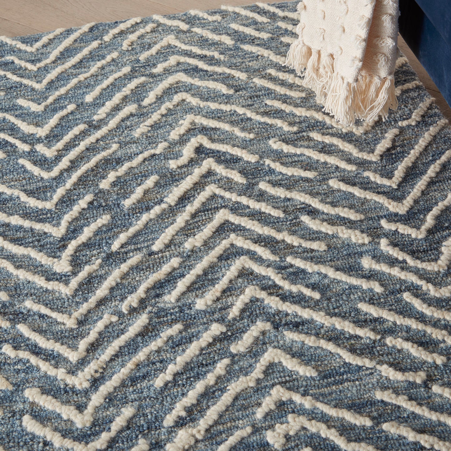 Blue and ivory tufted rug with white raised chevron/maze pattern; beige fringed throw draped at edge.