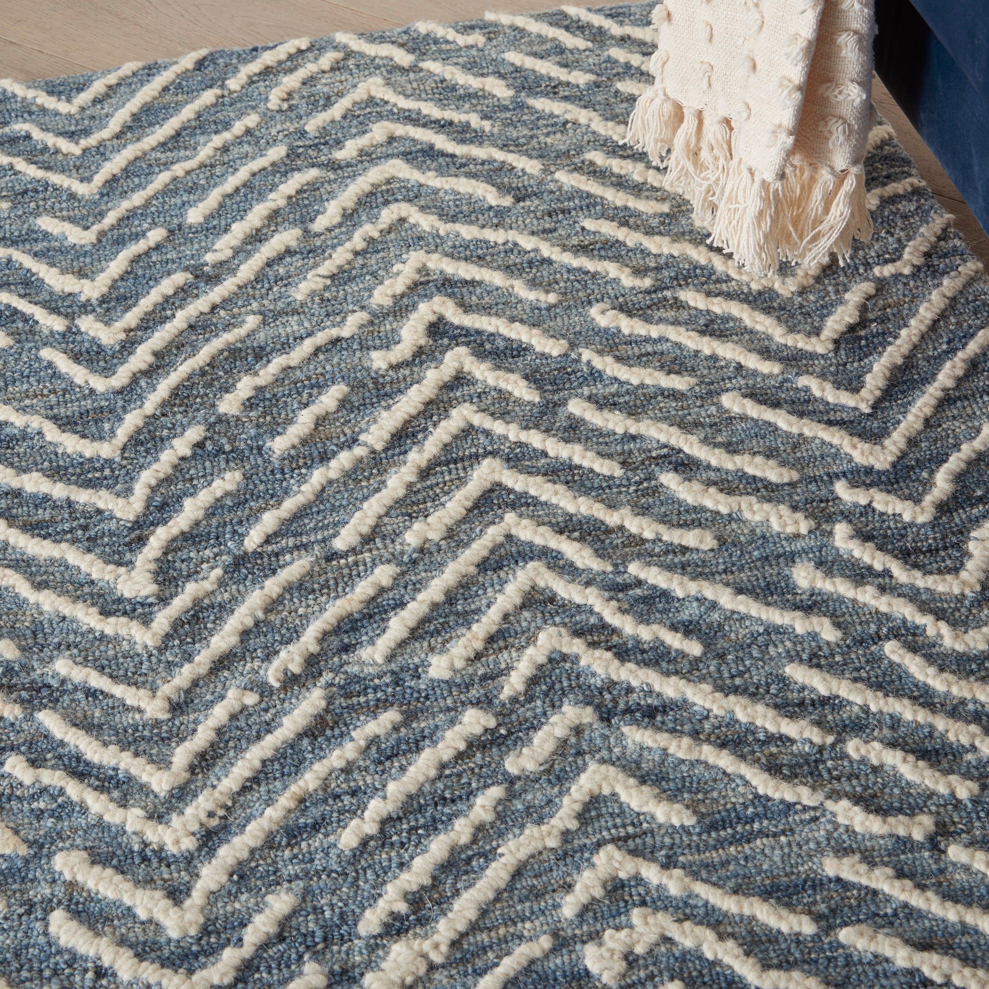 Blue and ivory tufted rug with white raised chevron/maze pattern; beige fringed throw draped at edge.