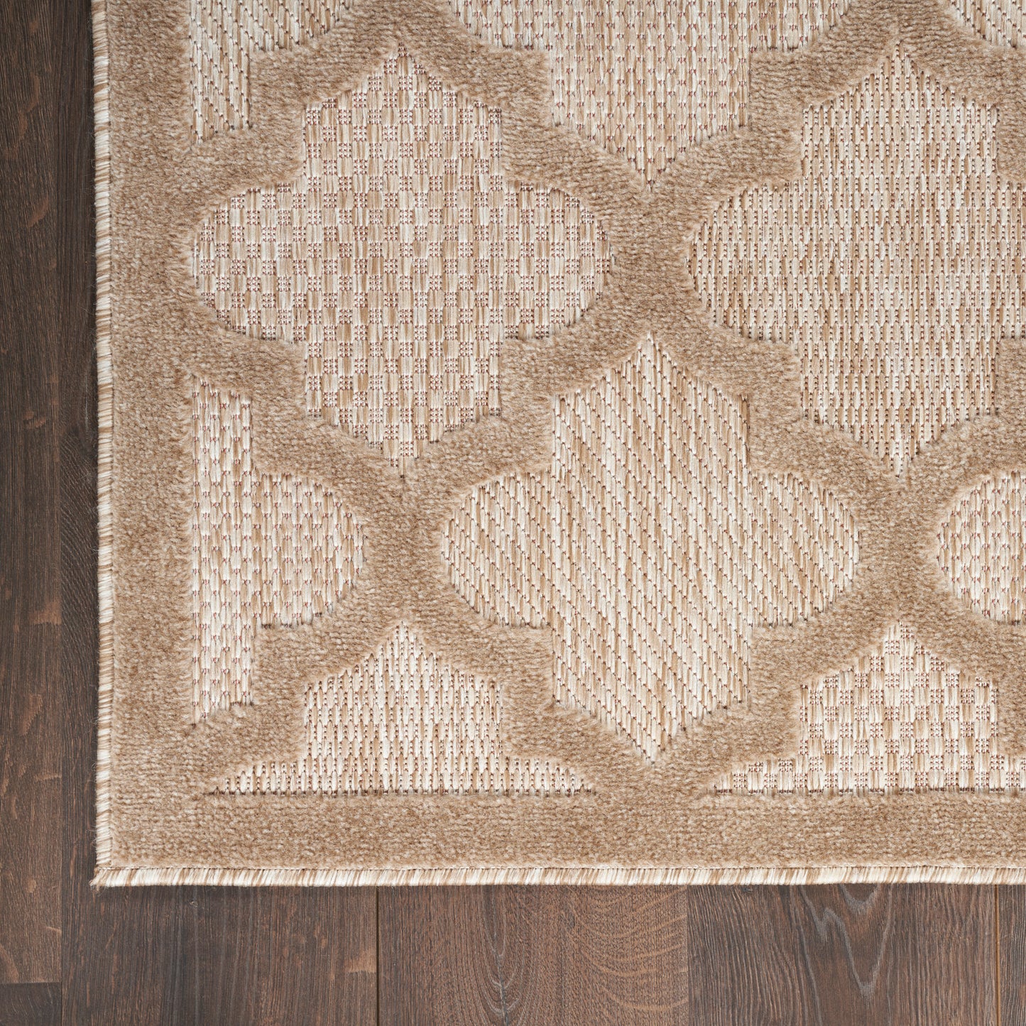 Beige and tan woven rug with a raised quatrefoil lattice pattern and bordered edge on dark wood floor.