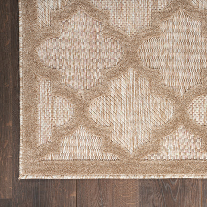 Beige and tan woven rug with a raised quatrefoil lattice pattern and bordered edge on dark wood floor.