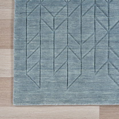 Blue-gray geometric area rug with chevron pattern and subtle texture on light wood floor.
