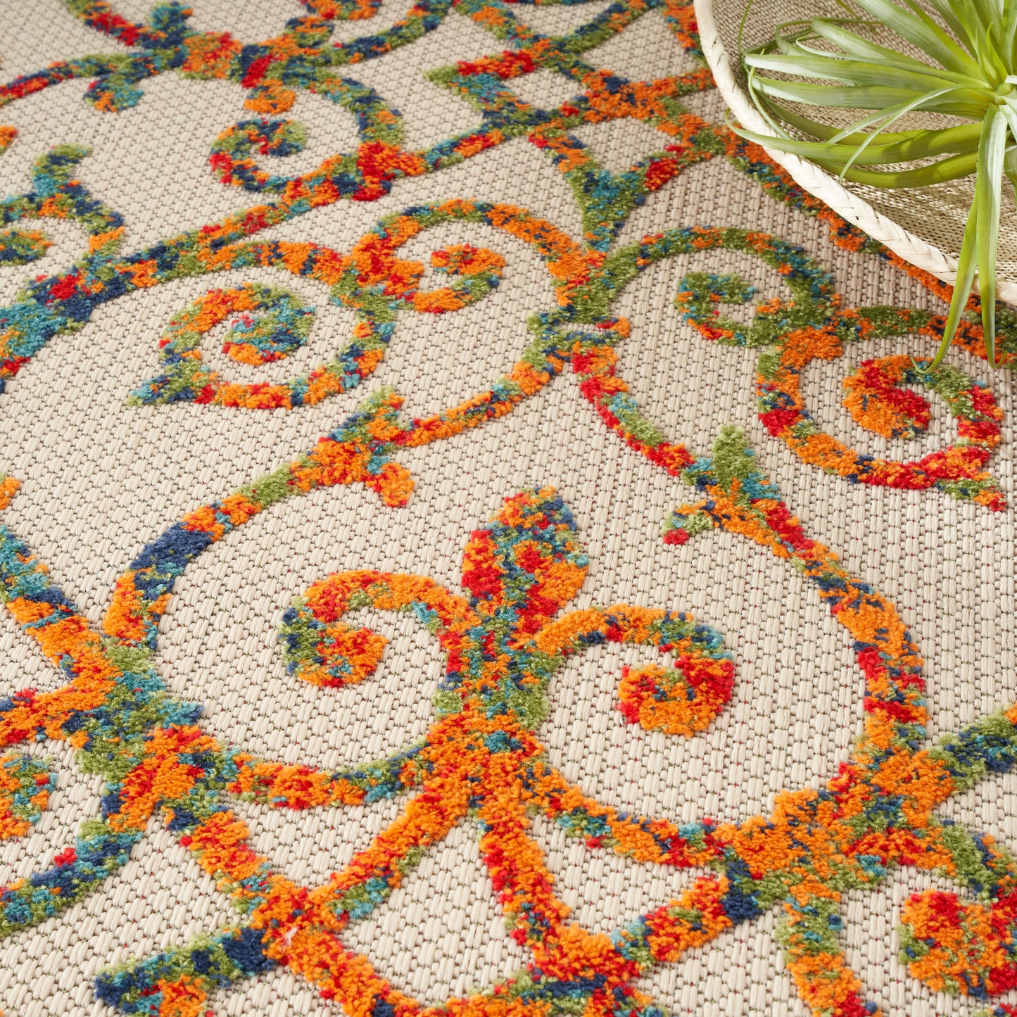 Beige area rug with vibrant orange, teal, blue and red scrolling pattern; woven textured surface.