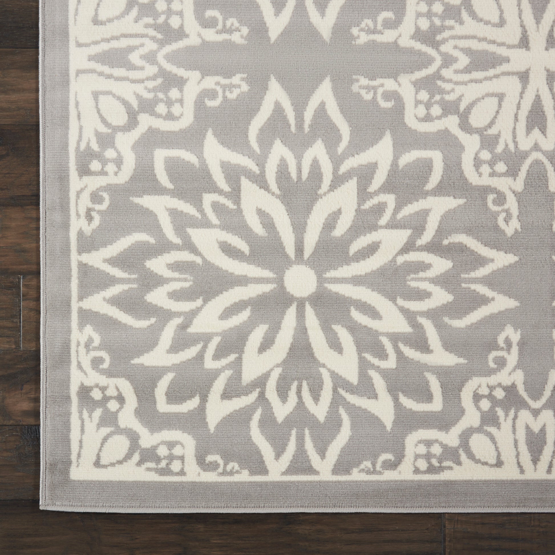 Gray rug with a large white floral mandala medallion and decorative border, flat-woven on a dark wood floor.