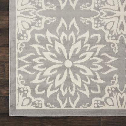 Gray rug with a large white floral mandala medallion and decorative border, flat-woven on a dark wood floor.
