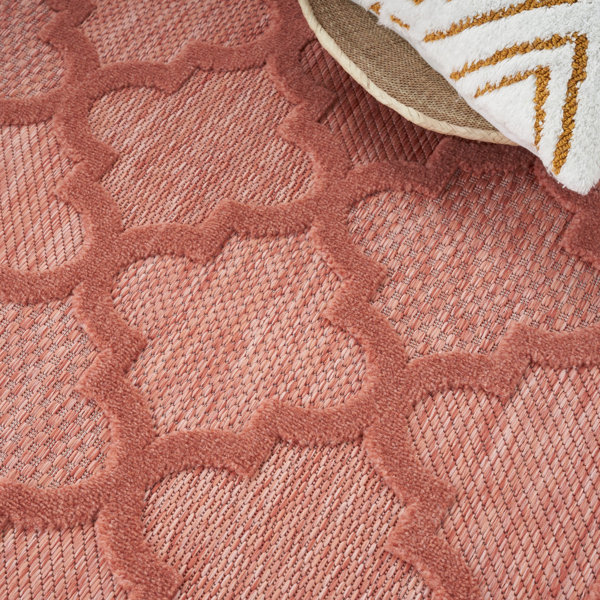 Rose-pink tufted rug with raised geometric trellis pattern; corner shows white towel with gold chevron design.