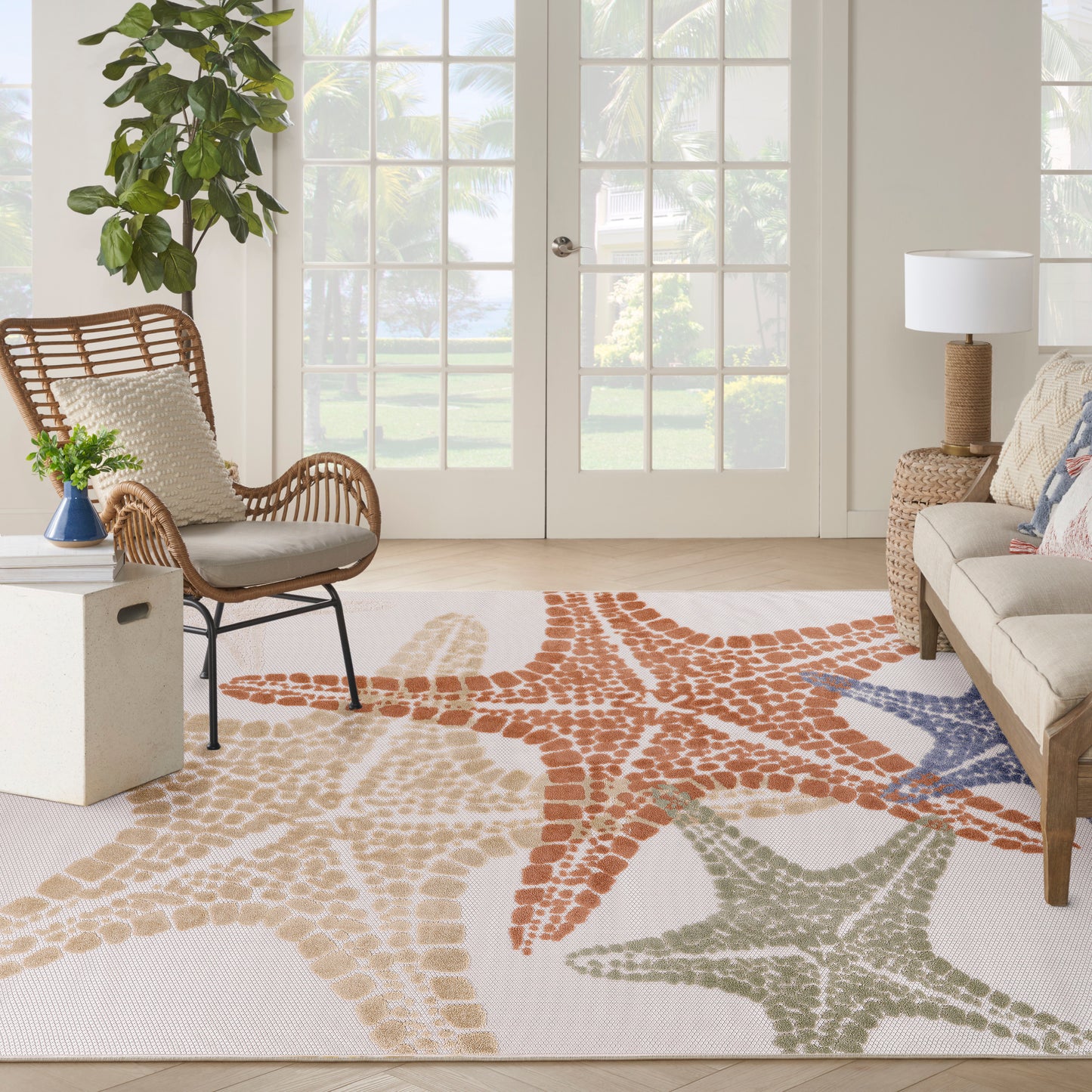Bright outdoor living area with an 8' x 11' woven coastal starfish rug in orange, beige, sage green & blue; rattan chair & cream sofa.