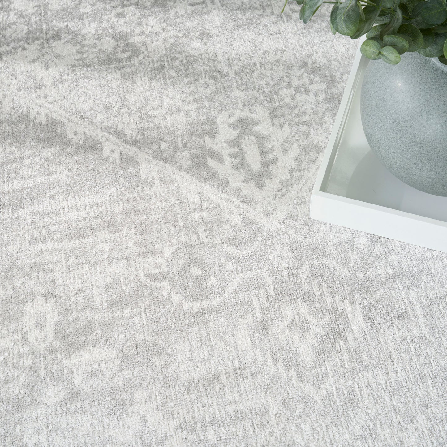 Light gray patterned rug with a white tray holding a gray ceramic pot and green plant.