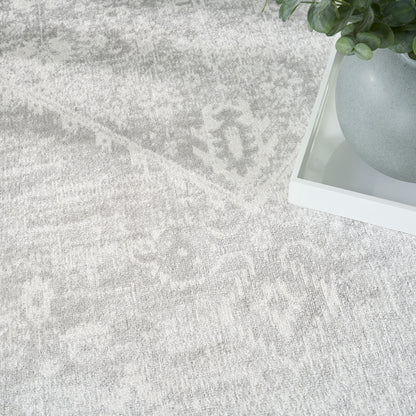 Light gray patterned rug with a white tray holding a gray ceramic pot and green plant.