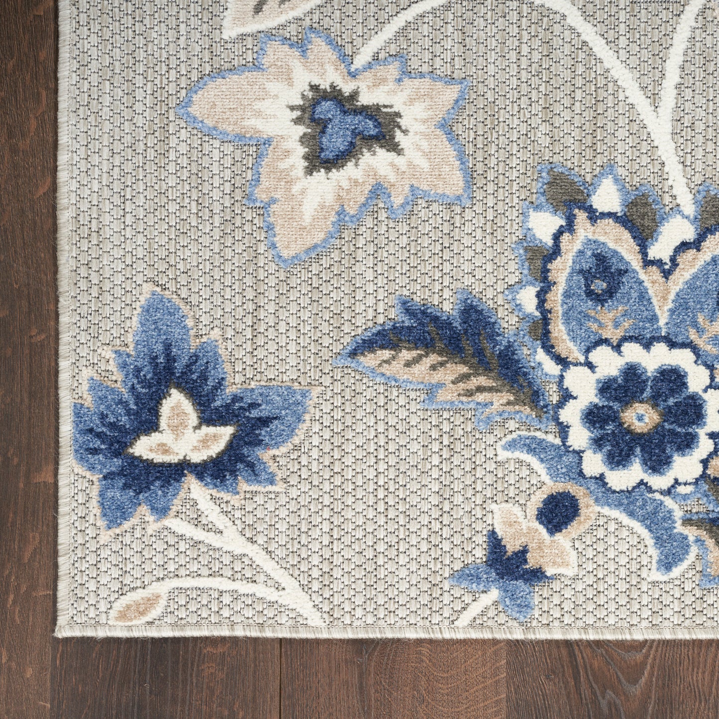 Rectangular gray-beige woven rug with blue and cream floral pattern; wood floor edge visible; 8' x 11'.