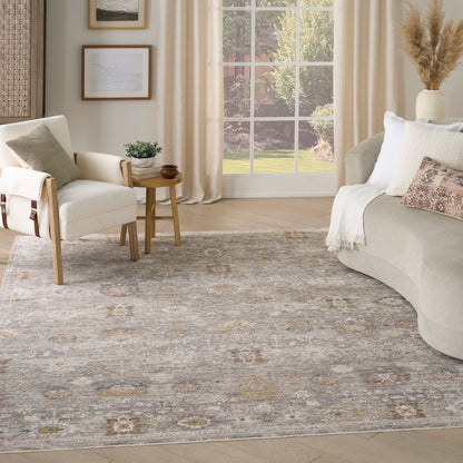 Neutral living room with cream sofa, round side table, light wood chair, and a muted floral-gray area rug by a large window.