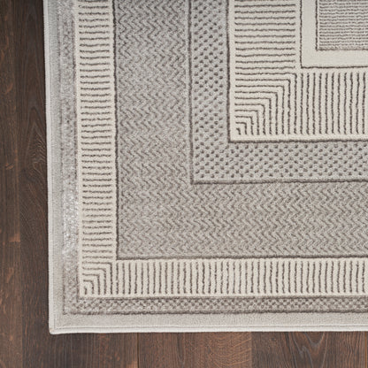 Rectangular woven area rug in neutral gray with layered chevron and stripe borders on a wood floor.