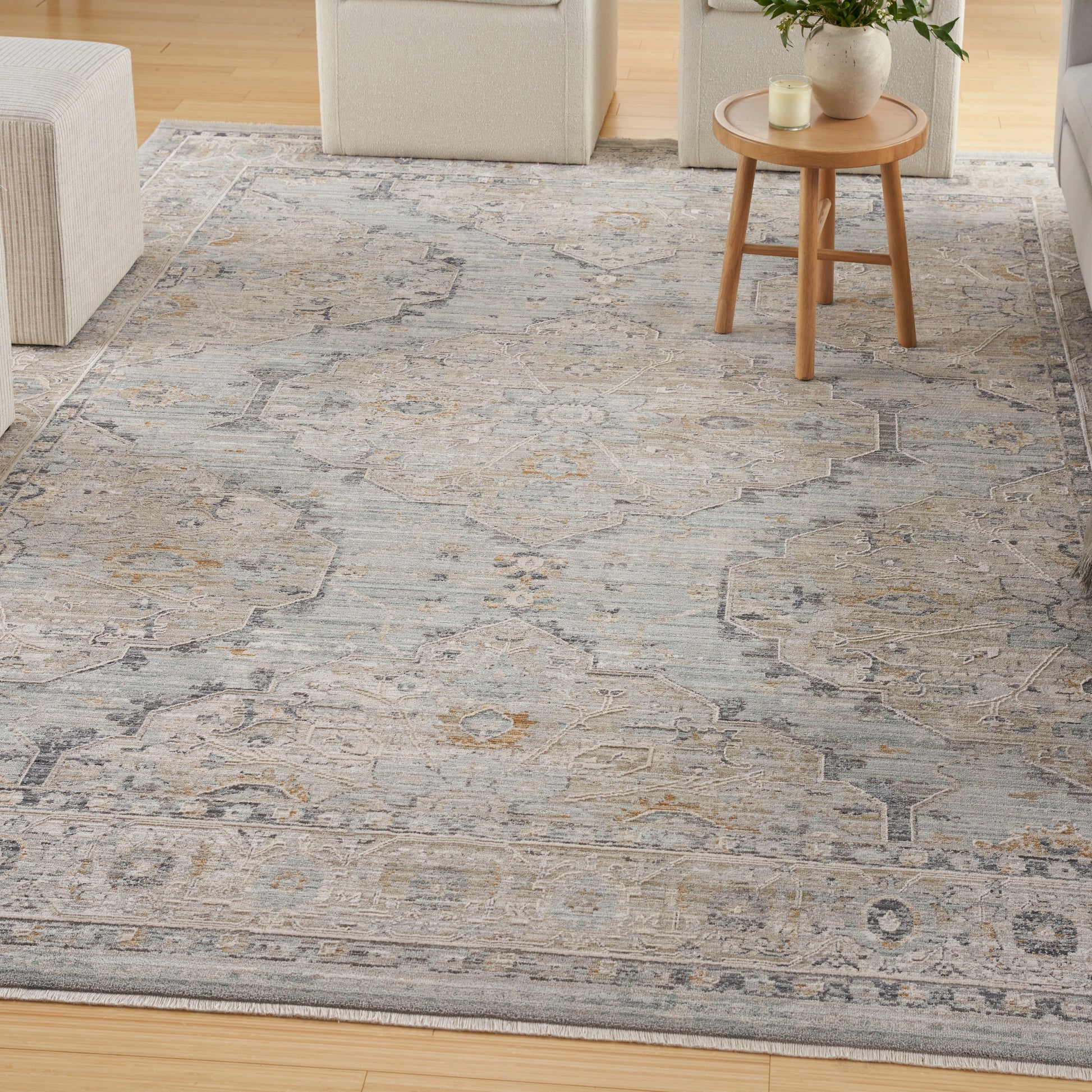 Gray-blue distressed oriental area rug with geometric motifs; beige seating and round wooden side table on light hardwood.