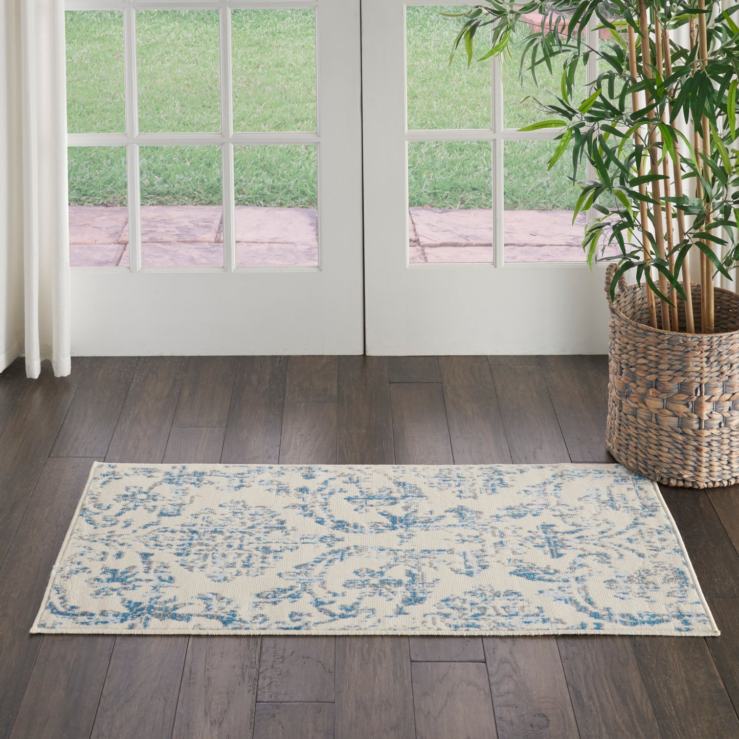 Light beige and blue patterned area rug on dark wood floor in front of French doors; potted plant in a woven basket to the right.