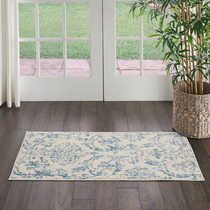 Light beige and blue patterned area rug on dark wood floor in front of French doors; potted plant in a woven basket to the right.