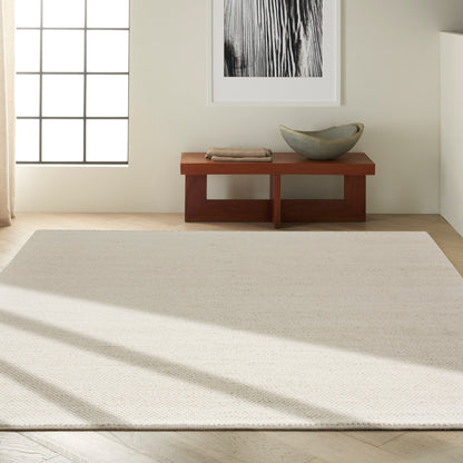 Minimalist living room with a cream rug, light wood floor, low reddish-brown bench, ceramic bowl, folded towels, framed black-and-white art.