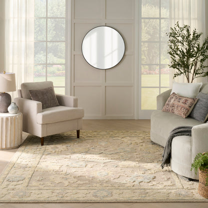 Neutral living room with beige sofa and armchair, round wall mirror, cream patterned rug, tall plant.