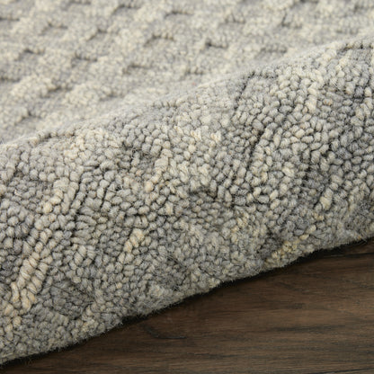 Close-up of a gray and ivory loop-pile rug with dense textured fibers, rolled edge on a dark wooden floor.