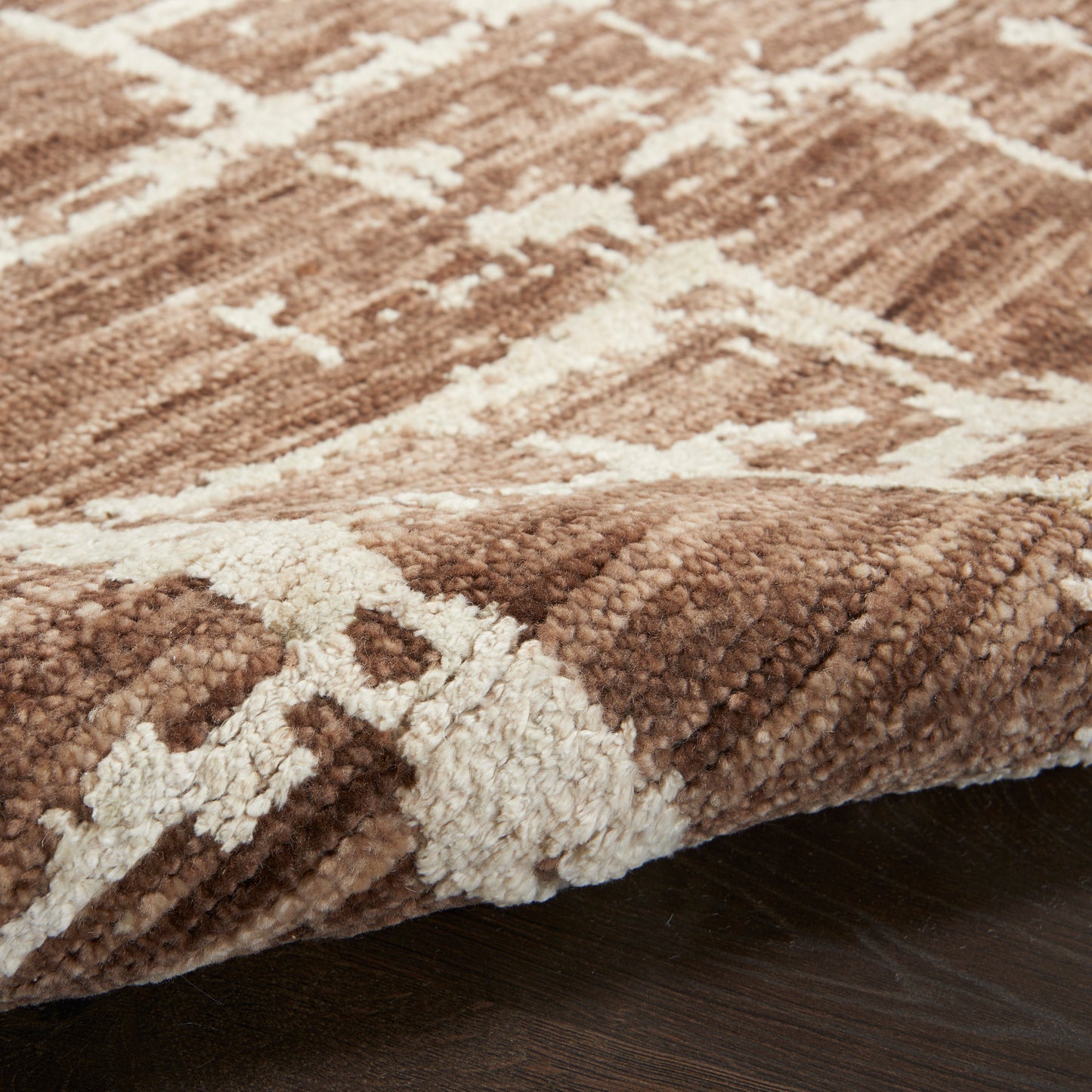 Brown and cream geometric rug with plush shaggy pile on dark wood floor.