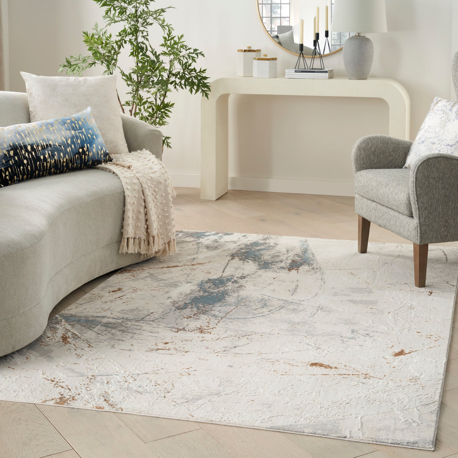 Soft neutral area rug with abstract blue-gray and tan pattern in a modern living room with a curved light-gray sofa.