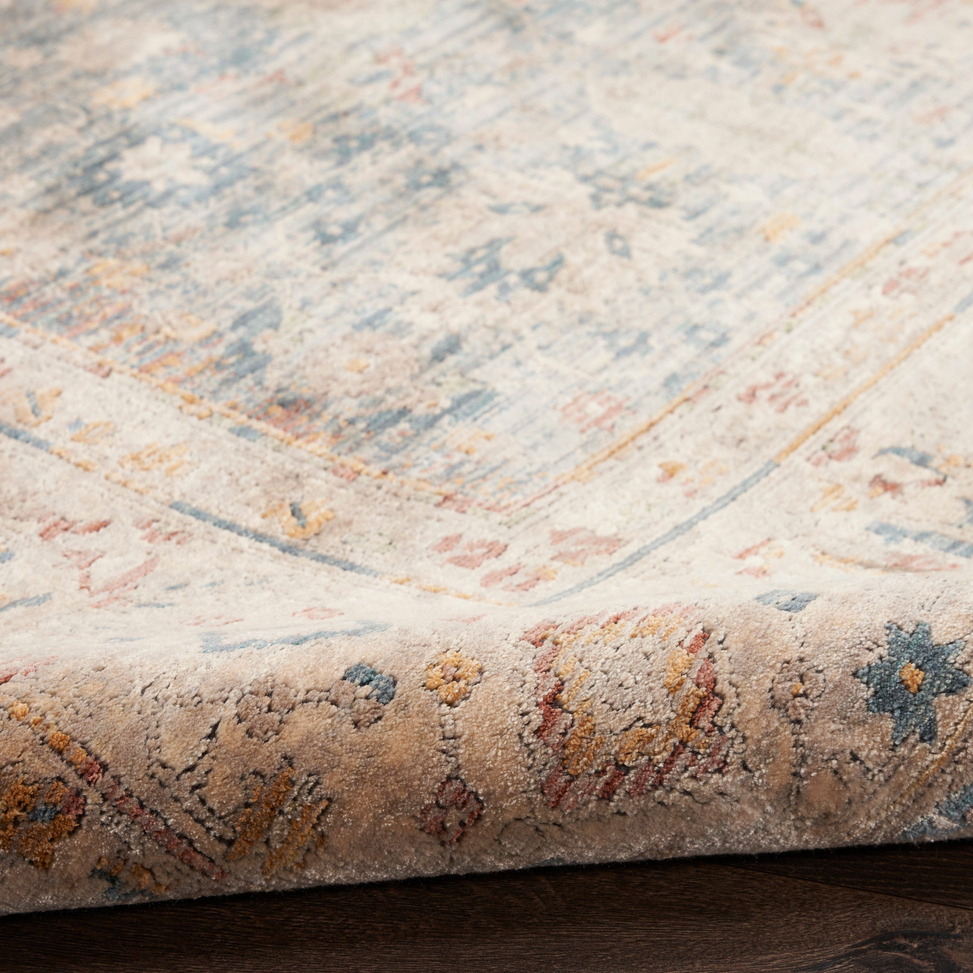 Pastel distressed area rug with beige base and blue, pink and yellow floral motifs; rolled edge reveals decorative border.