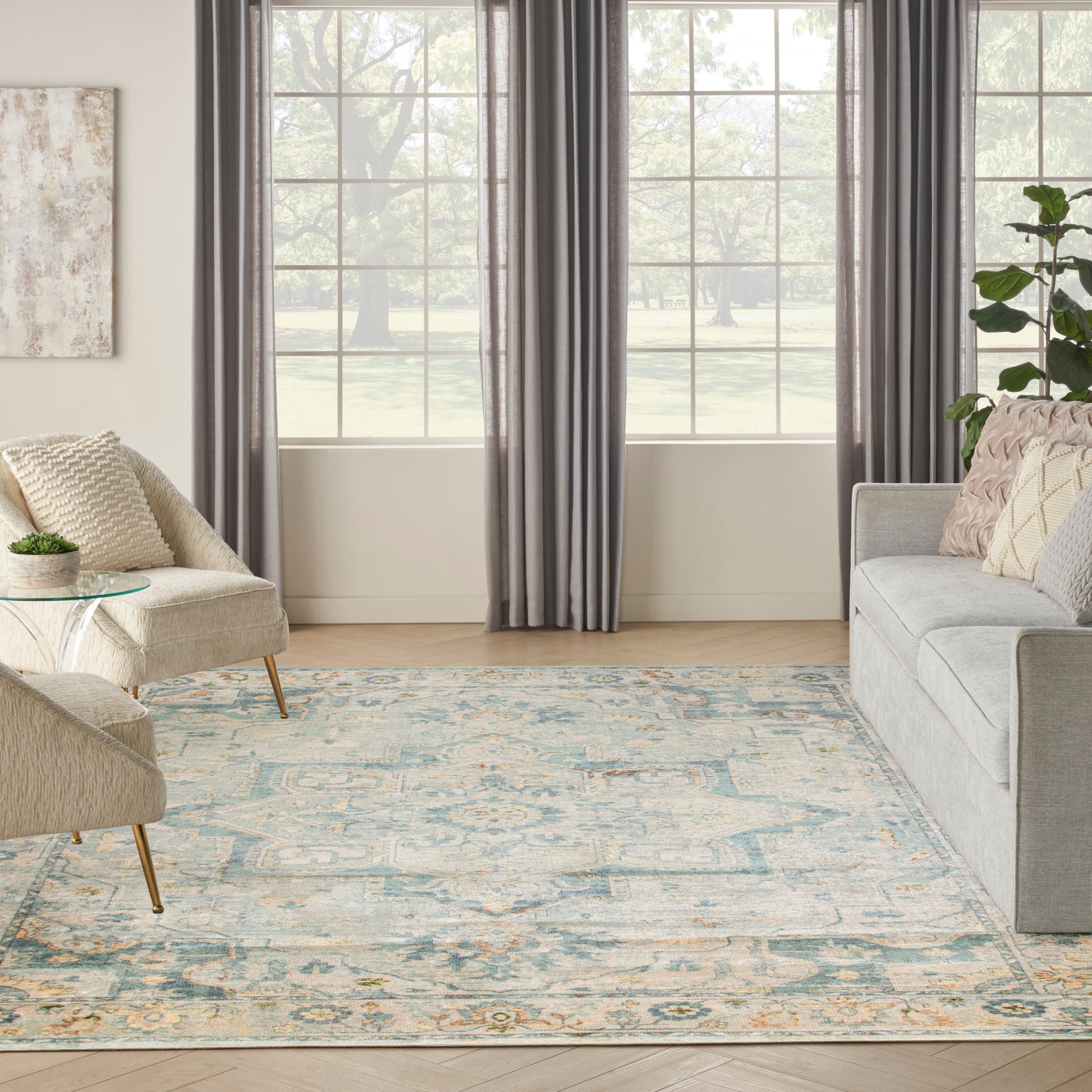 Bright living room with window, gray curtains, beige sofa and armchair, glass coffee table, and blue-gray patterned rug.