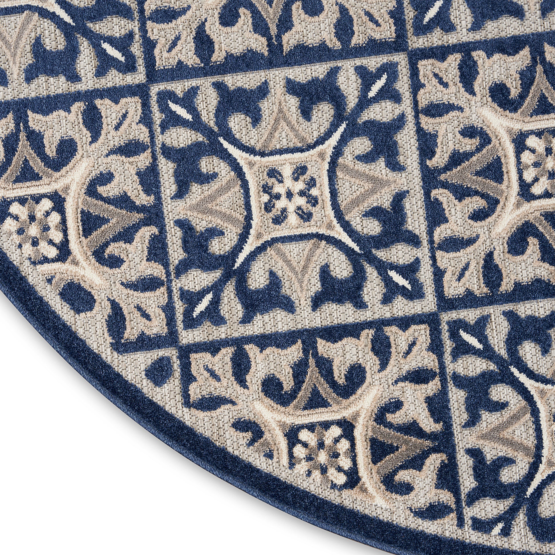 Blue and beige woven round rug with tile-like square motifs, floral vines, and a navy border.