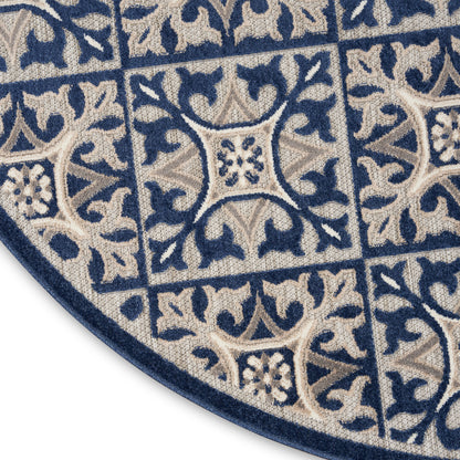 Blue and beige woven round rug with tile-like square motifs, floral vines, and a navy border.