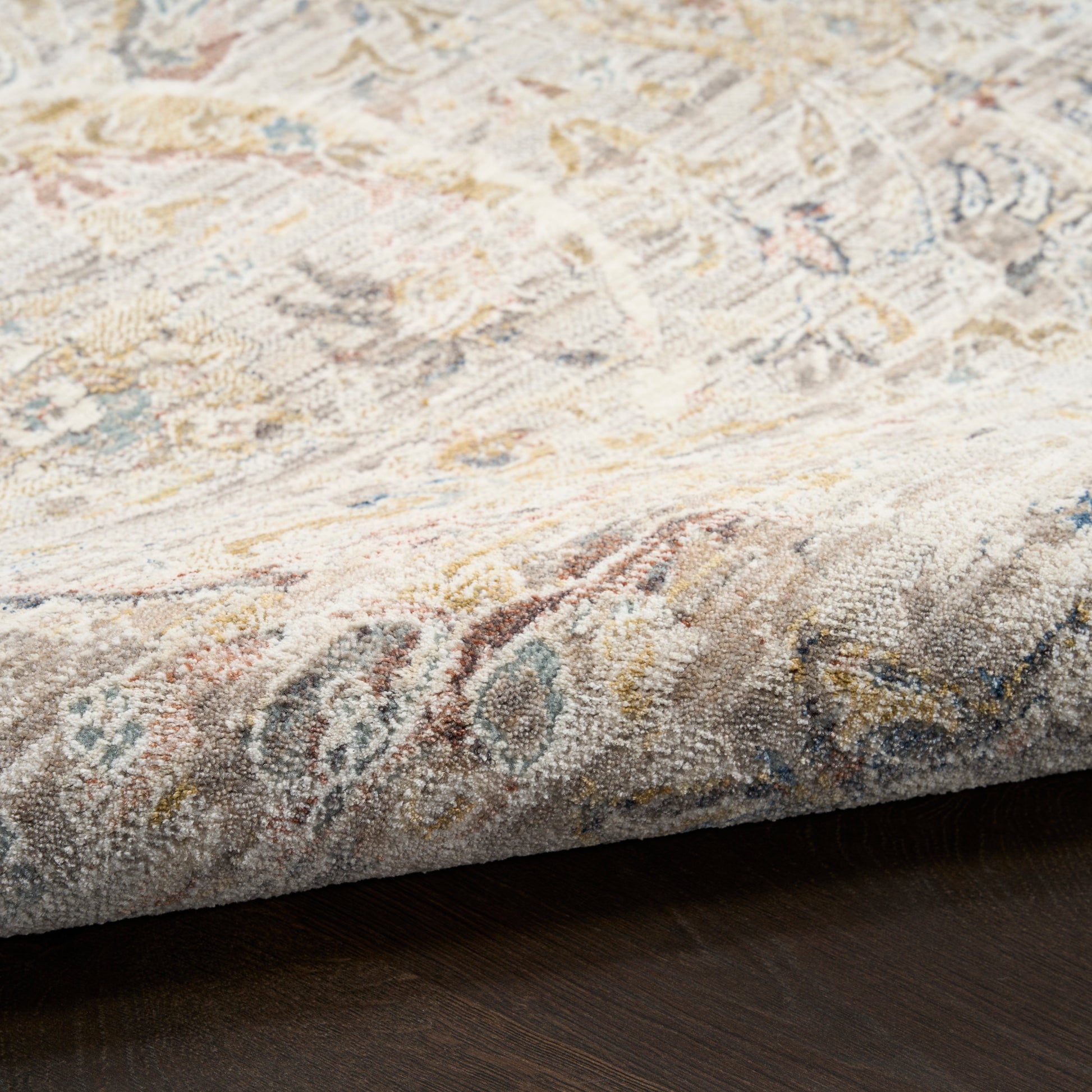 Close-up corner of a vintage-style woven runner rug with cream, beige, blue and gold tones on dark wood floor