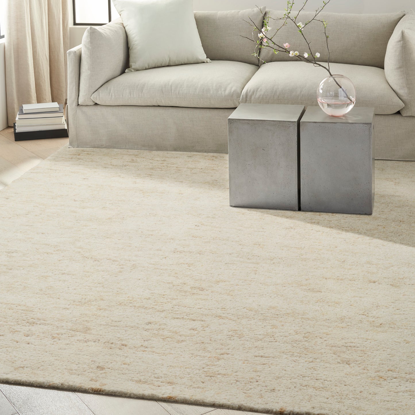 Neutral living room: cream-beige rug, light gray sofa, pair of square concrete side tables, glass vase with branch.