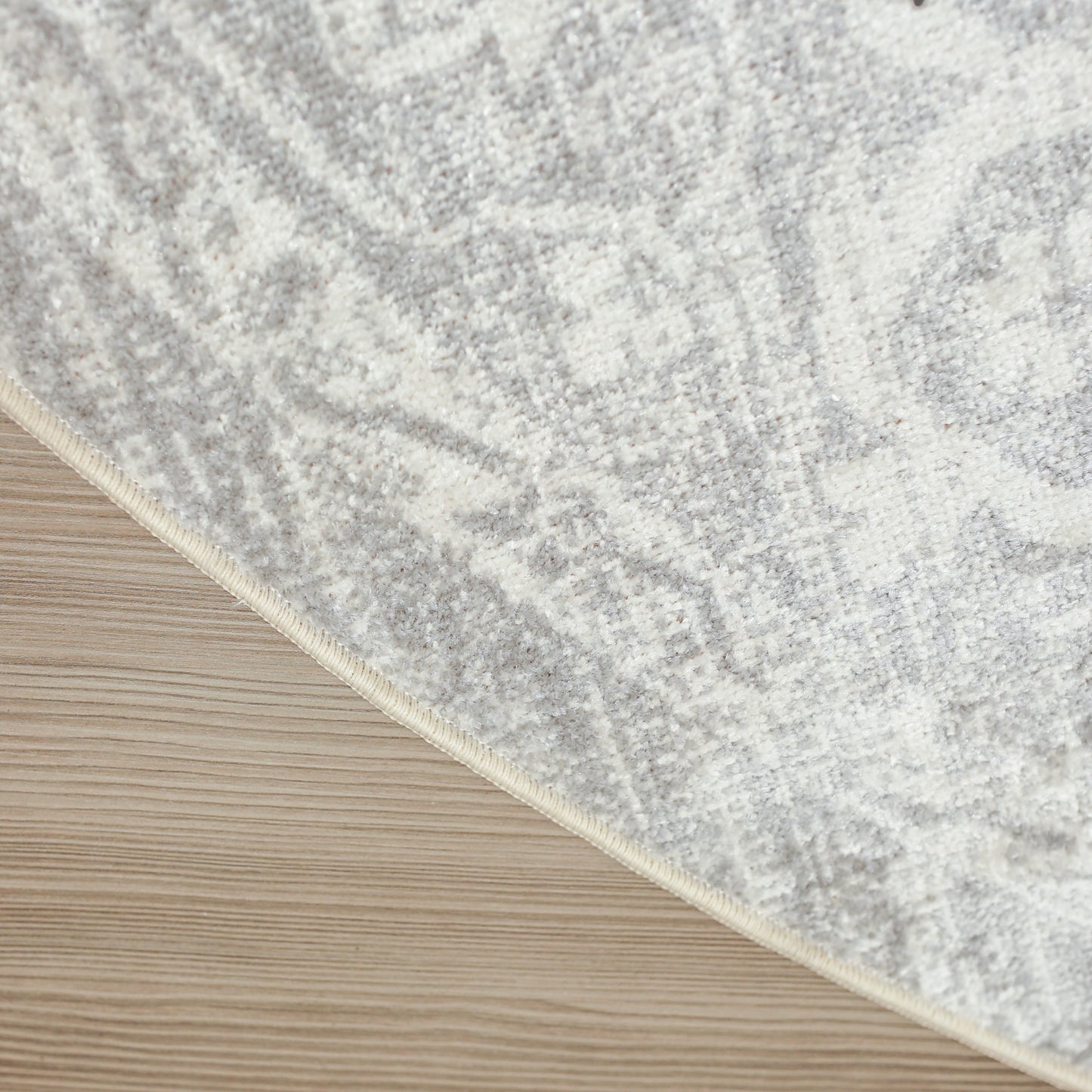 Soft gray and ivory patterned rug with beige edge binding on light wood floor.