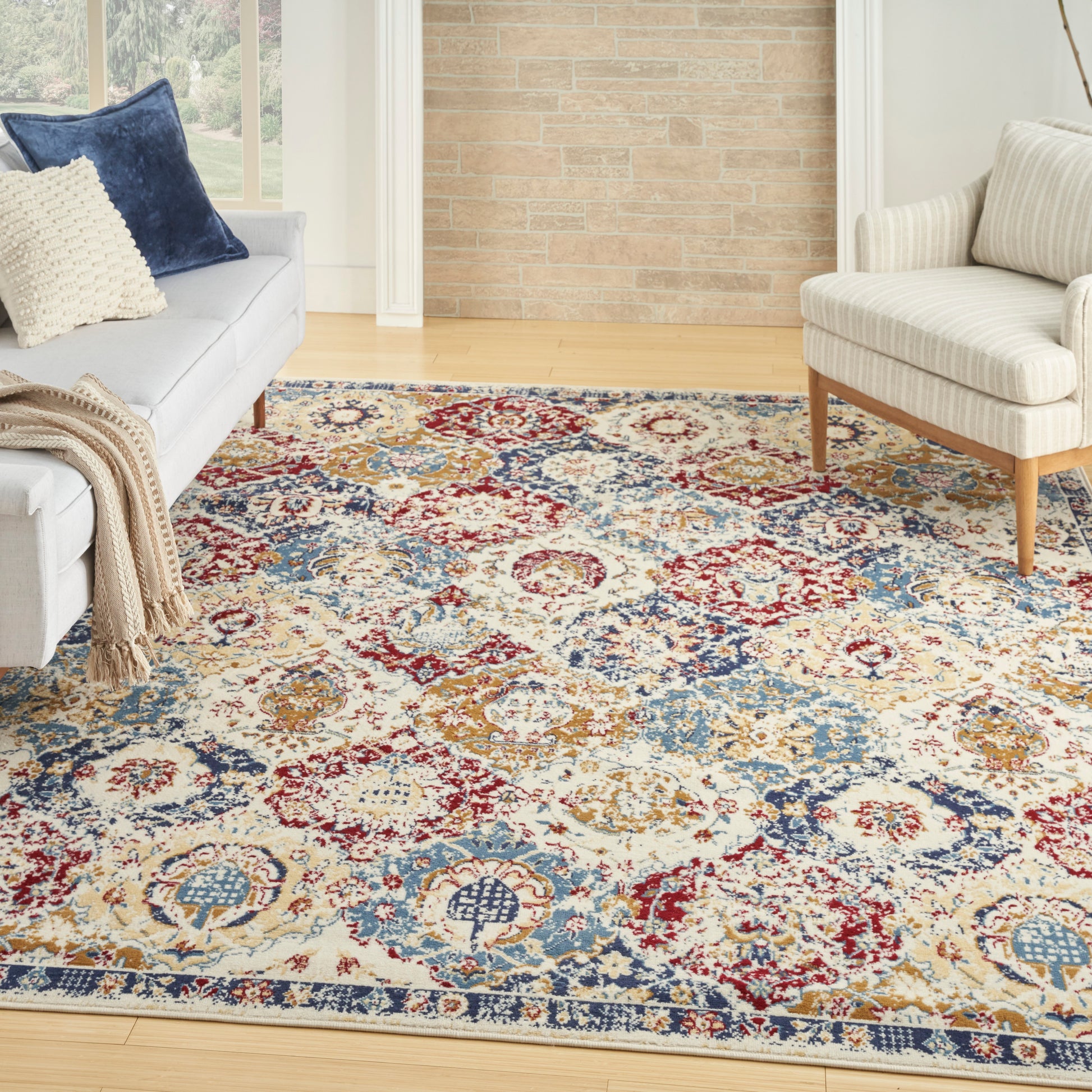Living room with a colorful ornate area rug, light gray sofa with blue and cream cushions, beige armchair, wood floor.