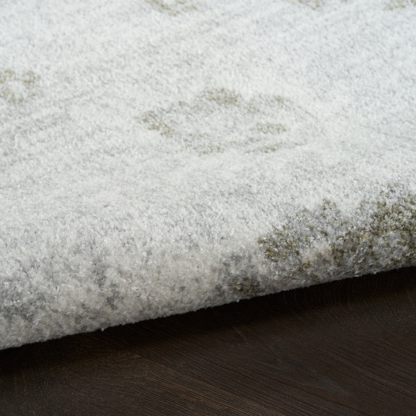 Soft light-gray plush area rug with subtle ivory floral motif; rectangular and resting on a dark wooden floor.