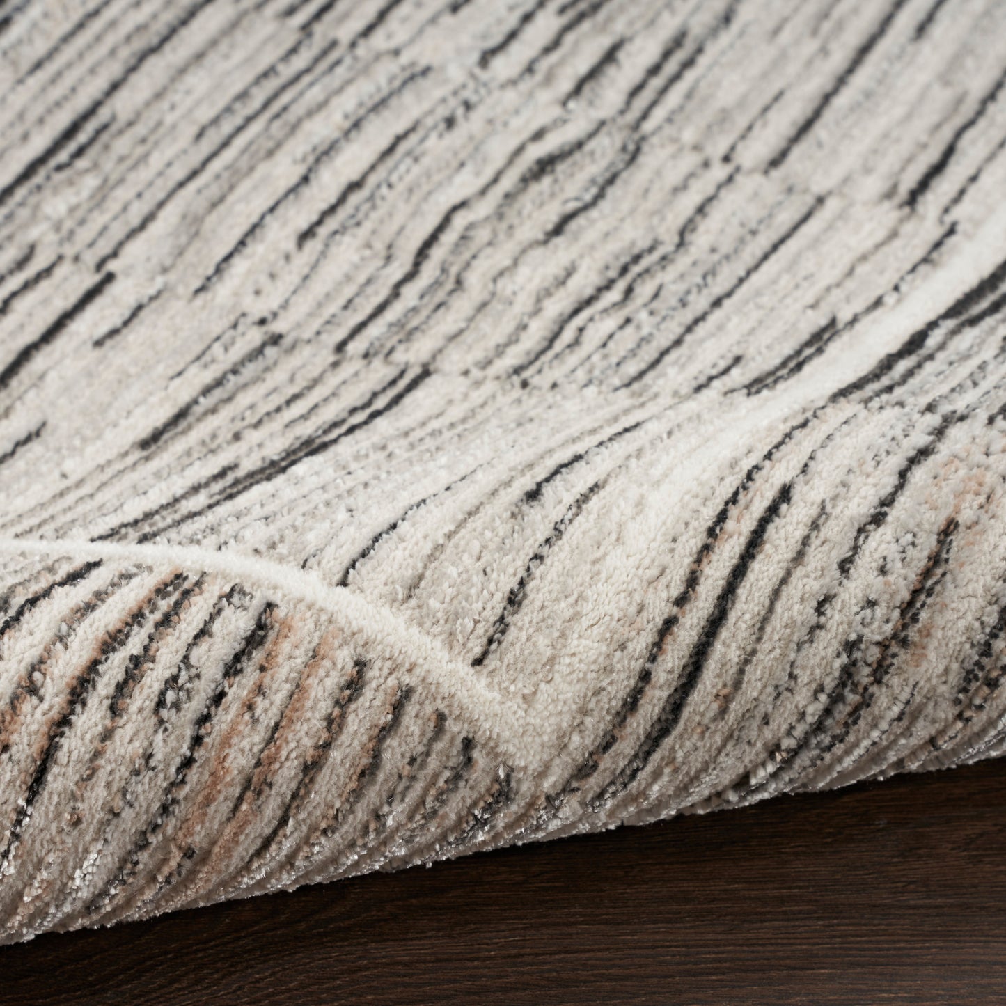 Beige cream rug with black linear stripes and plush pile, folded edge on dark wood floor.