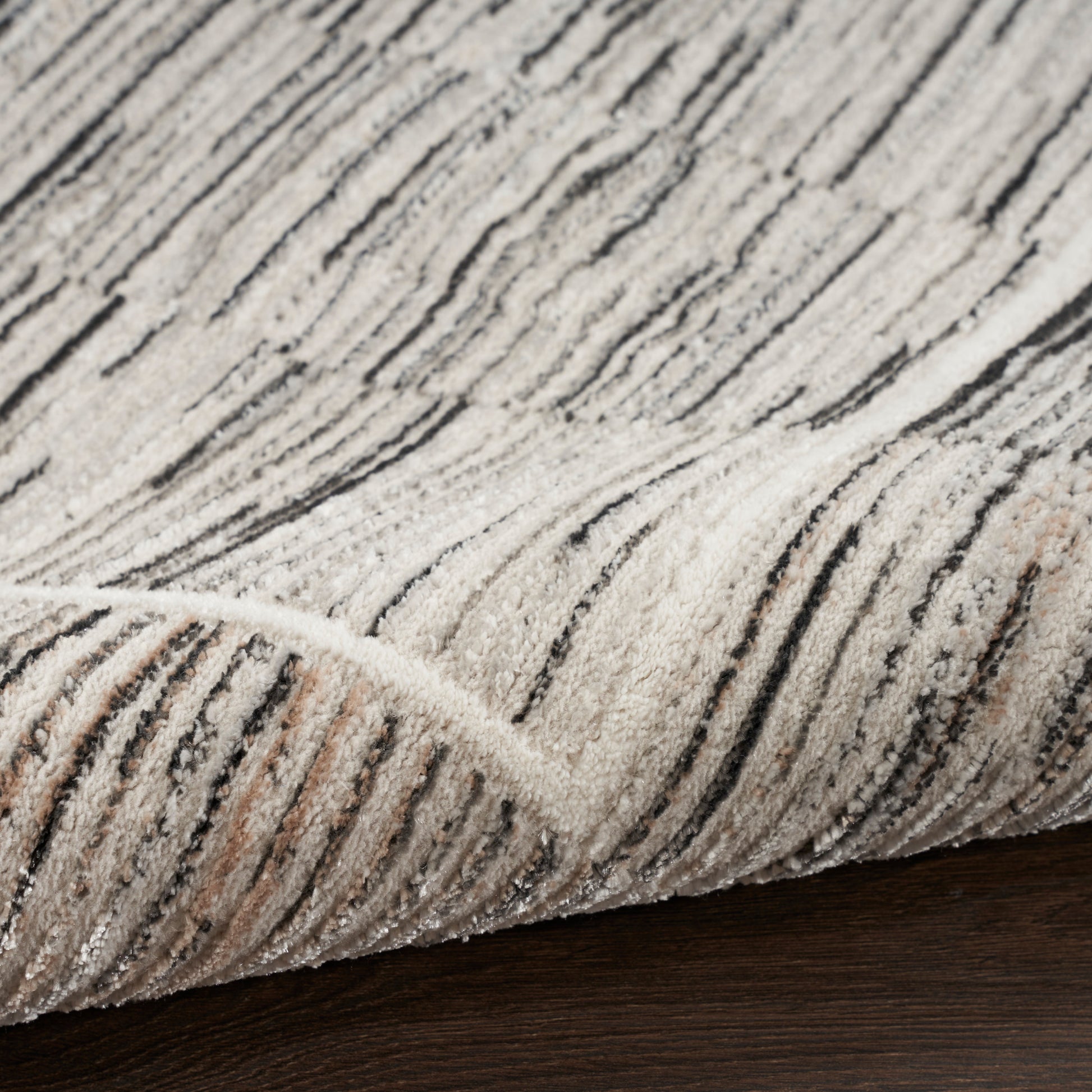 Beige cream rug with black linear stripes and plush pile, folded edge on dark wood floor.