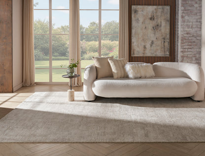 Cream curved fabric sofa with plush cushions in a sunlit contemporary living room with a beige rug