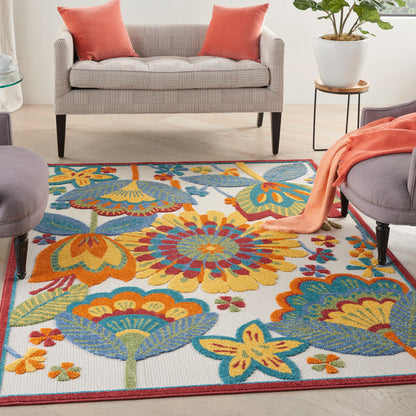 Colorful woven floral area rug on light wood floor; grey sofa with orange pillows, peach throw, and potted plant nearby.