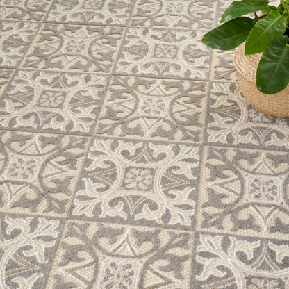 Gray-beige patterned area rug with ornate tile-like squares; plant in a woven basket sits in the corner.